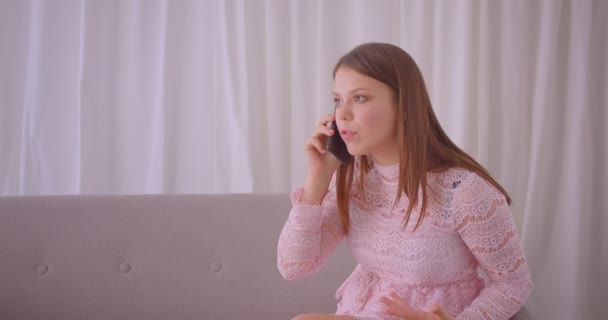 Closeup portrait of young attractive caucasian female having phone call talking cheerfully sitting on couch indoors in apartment — Stock Video