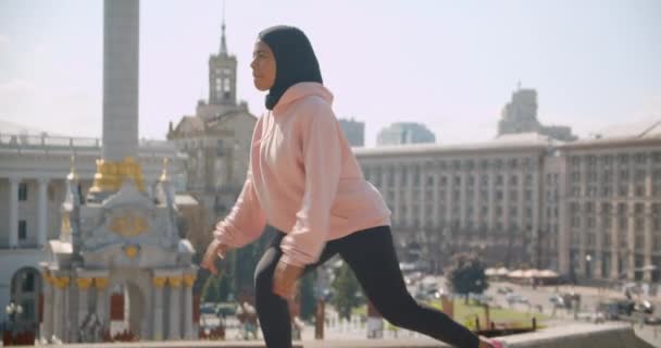 Closeup portrait of young attractive african american muslim girl in hijab stretching in urban city outdoors with buildings on background — Stock Video