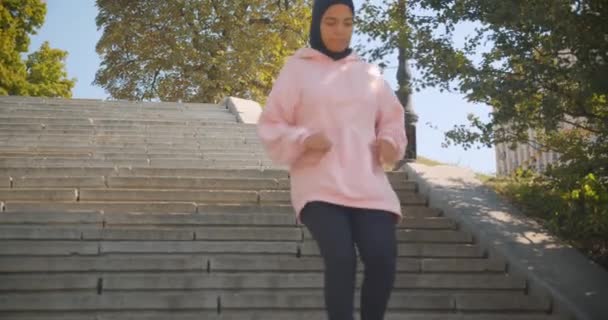 Крупный план портрета молодой привлекательной африканской мусульманки, бегающей трусцой и спускающейся вниз в городской части города — стоковое видео
