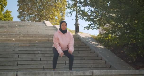 ヒジャーブの若い魅力的なアフリカ系アメリカ人イスラム教徒の女の子のクローズアップ肖像画は、屋外の都市都市の階段でカーディオを行います — ストック動画
