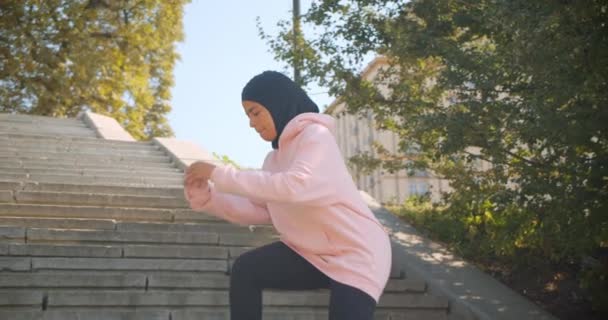Крупный план портрета молодой африканской мусульманской девушки в хиджабе, выпавшей на лестнице в городском городе на свежем воздухе — стоковое видео
