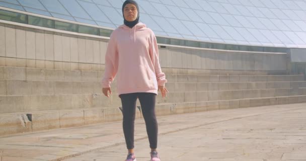 Nahaufnahme Porträt einer jungen attraktiven afrikanisch-amerikanischen muslimischen Mädchen im Hijab hockt auf Stadion Stadt im Freien — Stockvideo