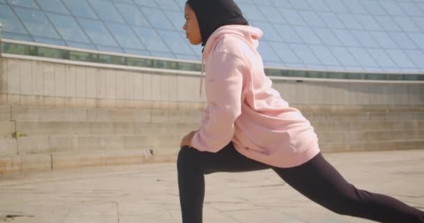 Närbild sida Visa porträtt av attraktiva afrikansk amerikansk muslimsk flicka i hijab stretching på arenan urbana staden utomhus — Stockvideo