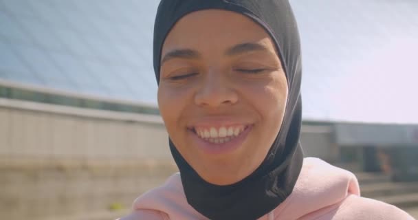 Closeup portré fiatal vonzó afro-amerikai muszlim lány hidzsáb nézi kamera mosolygó boldogan stadionban a városi város szabadtéri — Stock videók