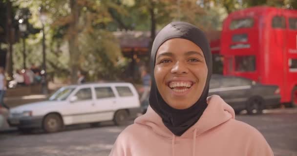 Türbanlı genç çekici afro-amerikan müslüman üniversiteli kızın closeup portresi şehir dışında mutlu bir şekilde ayakta gülümseyip gülüyor — Stok video