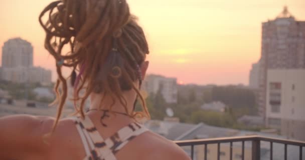 Closeup back view portrait of sporty female with dreadlocks doing yoga on rooftop with beautiful city landscape sunset on background — Stock Video
