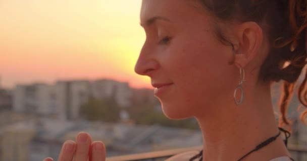 Κοντινά πλάνα πορτρέτο της πνευματικής καυκάσιας γυναίκας με ντρήλκς εξάσκηση γιόγκα χαμογελά χαρούμενα στην ταράτσα με όμορφο ηλιοβασίλεμα — Αρχείο Βίντεο