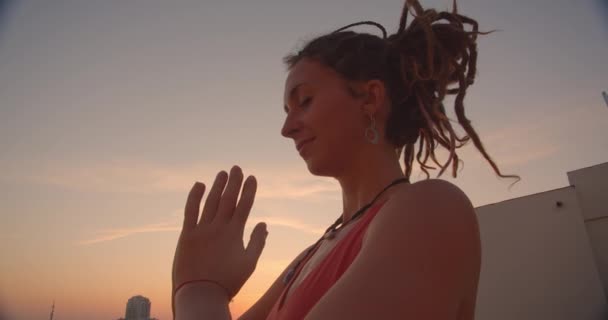 Closeup side view portrait of spiritual female with dreadlocks practicing yoga smiling happily on rooftop with beautiful city landscape on background — Stock Video