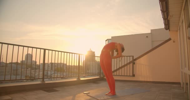 Closeup portrait of hipster female with dreadlocks practicing yoga stretching on rooftop with beautiful city landscape sunset on background — Stock Video