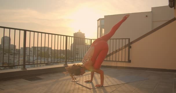 Närbild porträtt av flexibel hona med dreadlocks öva yoga asanas på taket i staden med vacker soluppgång på bakgrunden — Stockvideo