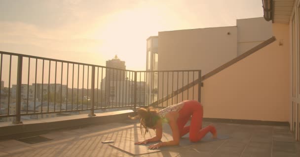 Retrato de cerca de una joven hembra con rastas practicando yoga en el balcón de la ciudad con hermoso amanecer en el fondo — Vídeo de stock