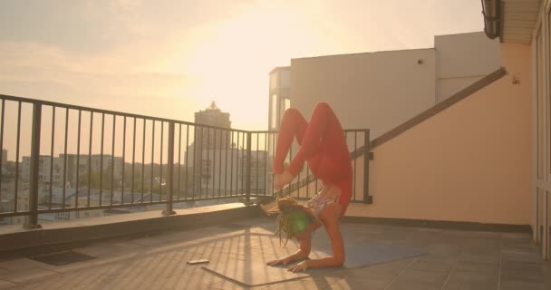 Gros plan portrait de jeune jolie femelle avec dreadlocks pratiquant le yoga sur le balcon en ville avec beau lever de soleil sur fond — Video