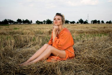 Sahada uzun turuncu elbiseli, zarif uzun bacaklı, gülümseyen güzel bir sarışın.