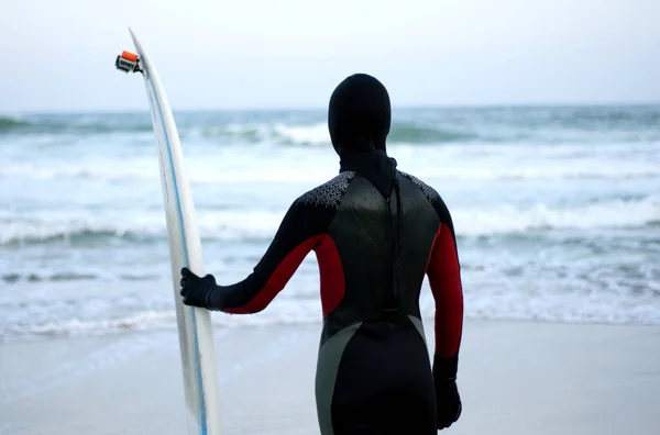 サーフボード付きのダイビングスーツのスポーツマンは 激しい海の背景に立っています サーフィン サーファー — ストック写真