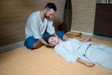 Masaj terapisti bir Tibet masaj için genç bir kadın yapıyor. erkek ve kadın beyaz jimnastik yapıyor. erkek ve kadın beyaz lotus içinde oturan konumlandırın ve rahatla