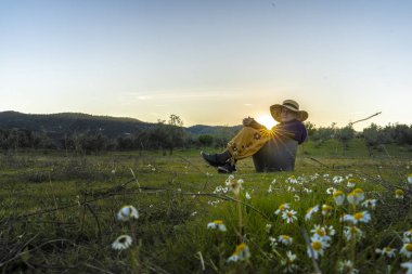 Hasır şapka alanında günbatımında oturan kadınla