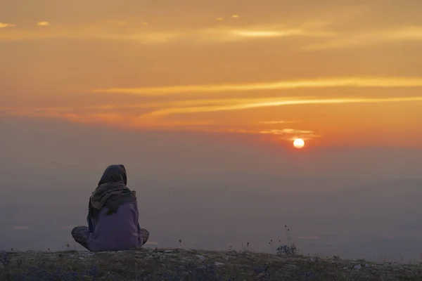 Woman with a scarf on her head sitting on top of a Subasio mount (Italy) watching the sunset