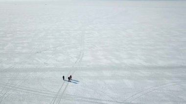 Alansal üç kişi yukarıdan dondurulmuş deniz boyunca yürümek. Kar-beyaz kutup çöl.