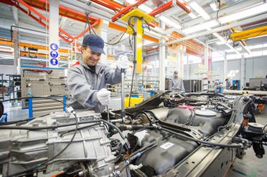 Otomotiv fabrikası. Bir büyük parlak atölyede sökülüp arabalar vardır.