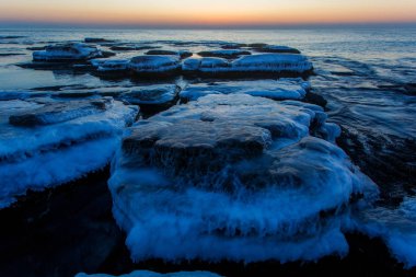 Güzel deniz manzarası. Buzla kaplı büyük kayalar şafak vakti deniz suyuyla doldu..
