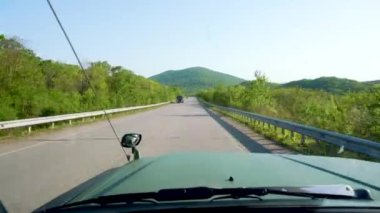 Arabanın ön camından görüntüyü al. Büyük yeşil bir cip, güzel manzaralı asfalt bir köy yolunda ilerliyor. Araba turizmi.