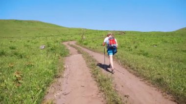 2019 yazında, Primorsky Krai, Rusya 'da yürüyüş direkleri olan genç bir erkek turist yeşil bir alanda toprak bir yolda yürüyor..