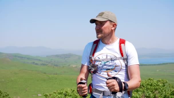 Summer, 2019 - Primorsky Krai, Russia - Young male tourist with trekking poles admires the surrounding views from a green hill. — Stock Footage Summer 2019 Primorsky Krai Russia Young Male Tourist Trekking Poles Royalty Free Stock Footage