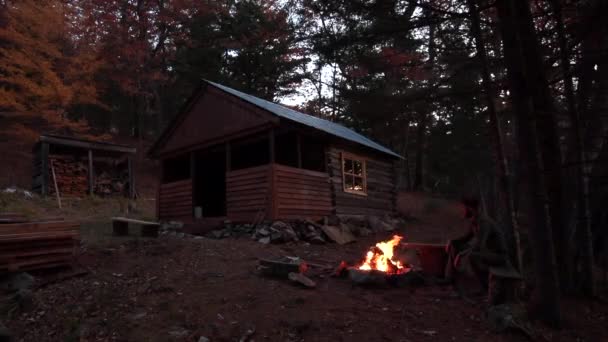 スローモーションだ暗闇の森の家を背に タイガの火のそばに座っている青年 — ストック動画