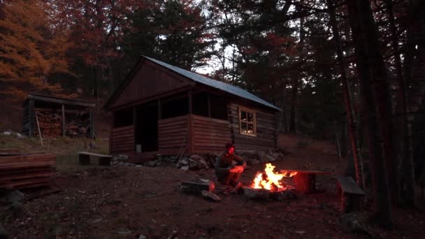 スローモーションだ暗闇の森の家を背に タイガの火のそばに座っている青年 — ストック動画