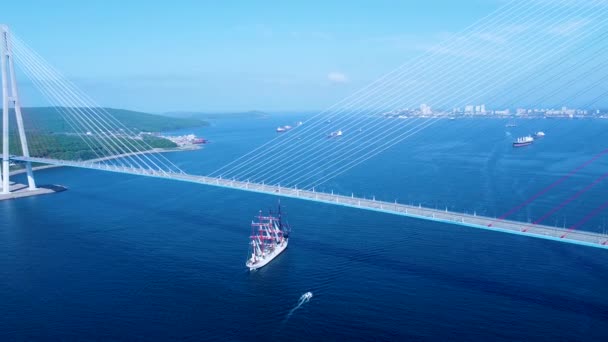上からの眺め ウラジオストクのロシア橋の下を雪のように白い帆船が通過します 東ボスポラス島に沿ってロシアの島を泳いで渡る帆船 — ストック動画