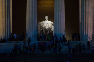 Lincoln Anıtı 'nda aydınlatılmış bir Lincoln heykeli. Turistler akşamları Lincoln heykelinin arka planında gezinirler.