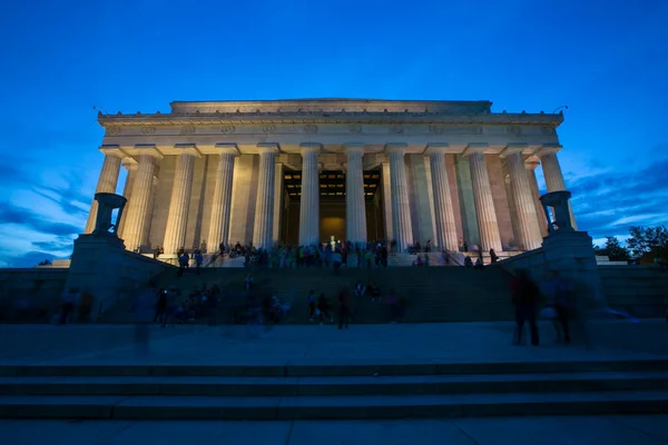 People wander around the Lincoln Memorial in the evening. Backlit Lincoln Memorial against a blue sky.