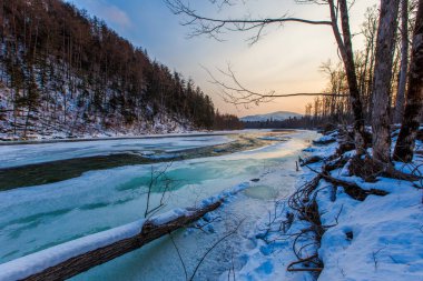 Primorsky bölgesinin kuzey manzarası, Samarga Nehri. Gün batımında ağaçlı tepelerin arka planında donmuş nehir.