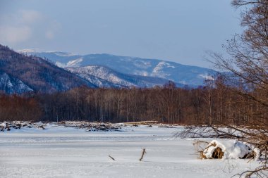 Primorsky bölgesinin kuzey manzarası, Samarga Nehri. Gün batımında ağaçlı tepelerin arka planında donmuş nehir.