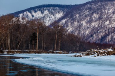 Primorsky bölgesinin kuzey manzarası, Samarga Nehri. Gün batımında ağaçlı tepelerin arka planında donmuş nehir.