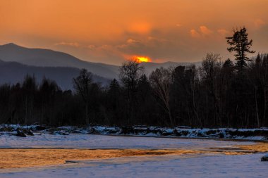 Primorsky bölgesinin kuzey manzarası, Samarga Nehri. Gün batımında ağaçlı tepelerin arka planında donmuş nehir.