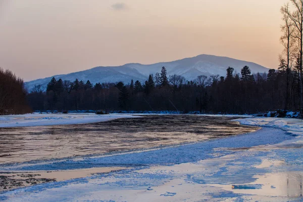 Primorsky bölgesinin kuzey manzarası, Samarga Nehri. Gün batımında ağaçlı tepelerin arka planında donmuş nehir.