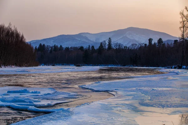 Primorsky bölgesinin kuzey manzarası, Samarga Nehri. Gün batımında ağaçlı tepelerin arka planında donmuş nehir.