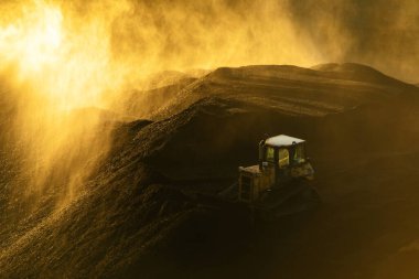 Buldozer, parlak şafak vakti püskürtücülerin önünde büyük bir kömür yığını üzerinde çalışır.