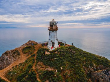 Yukarıdan. Primorsky Bölgesi, Smychka (Rudnaya Pristan) köyündeki Cape Briner 'daki Rudny deniz feneri. Güzel Rudny deniz feneri, parlak bir şafağın arkaplanına karşı dik bir uçurumda duruyor.