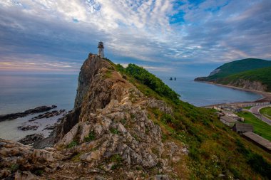Primorsky Bölgesi, Smychka (Rudnaya Pristan) köyündeki Cape Briner 'daki Rudny deniz feneri. Güzel Rudny deniz feneri, parlak bir şafağın arkaplanına karşı dik bir uçurumda duruyor.