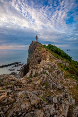Primorsky Bölgesi, Smychka (Rudnaya Pristan) köyündeki Cape Briner 'daki Rudny deniz feneri. Güzel Rudny deniz feneri, parlak bir şafağın arkaplanına karşı dik bir uçurumda duruyor.