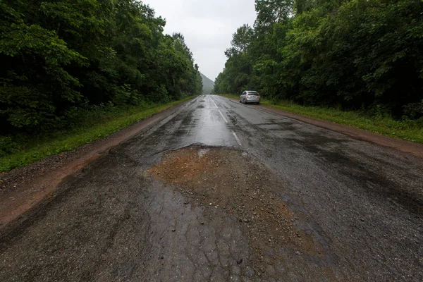 Very bad road in Russia. The asphalt road is all in holes in the middle of the forest.