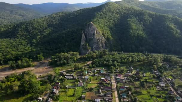 Pohled shora. Dersu rock ve vesnici Kavalerovo. Velká skála na pozadí kopců se zeleným lesem. Jednopodlažní vesnické domy na pozadí zelených hor a skal — Stock video