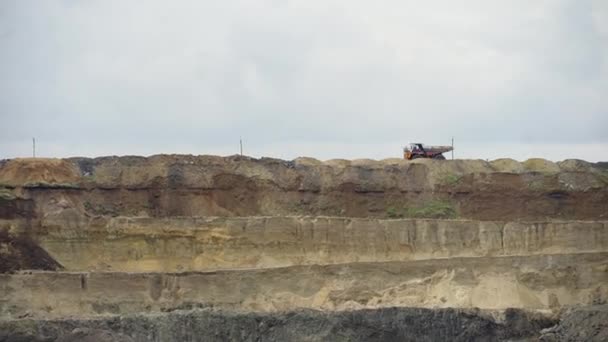 Belaz Amarilla atraviesa la cantera con un cuerpo cargado de tierra sobre el fondo de altos montones de tierra — Vídeos de Stock