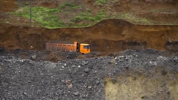 Un camión volquete atraviesa una cantera con un cuerpo cargado de tierra sobre el fondo de altos montones de tierra — Vídeos de Stock