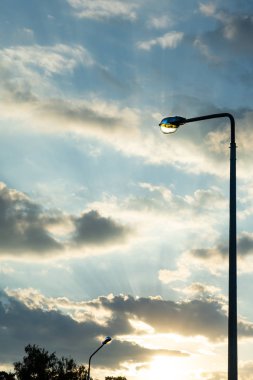 Akşam gökyüzü arka planda batan güneşin ışınları ile elektrik direği. Kopyala Yapıştır.