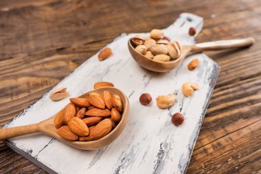 Koyu ahşap bir masa üzerinde tahta kaşıklar içinde fındık.