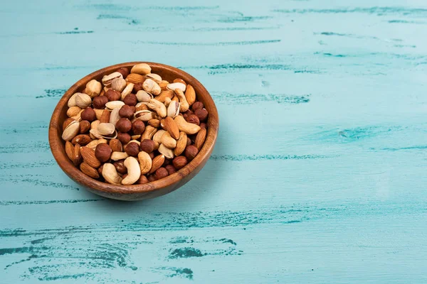 Mavi ahşap masa üzerinde ahşap kase fındık ürün yelpazesine. Kaju fıstığı, fındık, badem.
