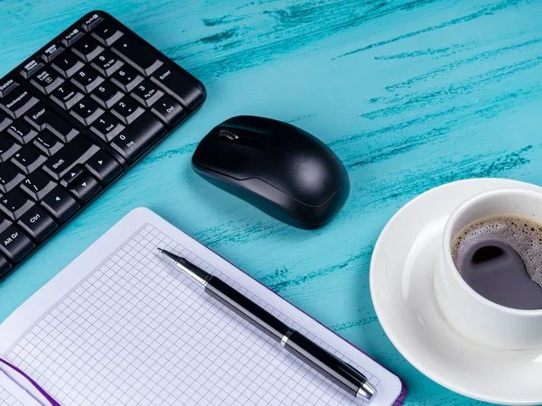 Escritorio de mesa de oficina. Espacio de trabajo con libreta de notas, teclado, útiles de oficina y taza de café sobre fondo de madera . — Foto de Stock